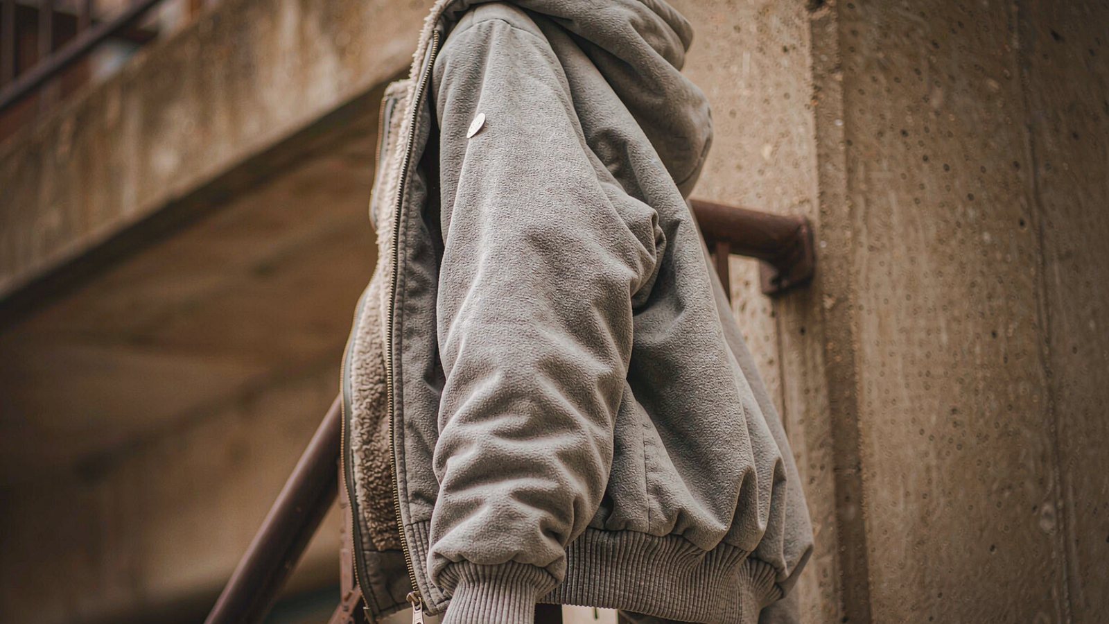 A thick grey hoodie draped over a metal railing in front of a painted urban wall under soft overcast light